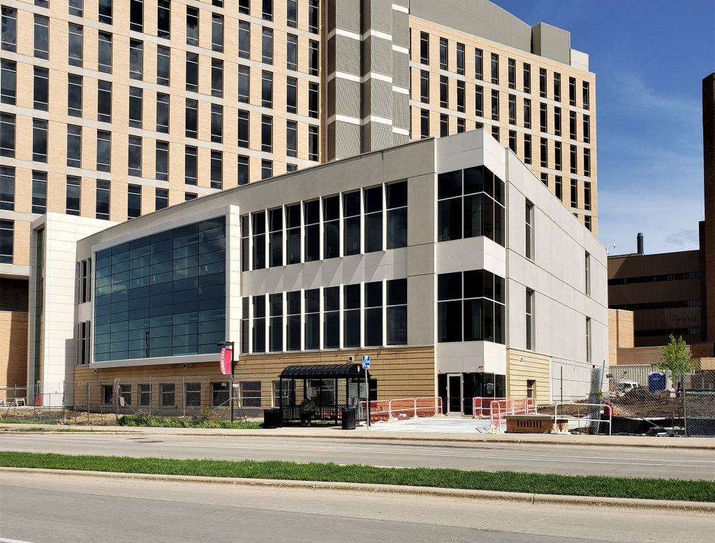 Modern multi‑story building with large windows and beige panels viewed from across a street under a clear blue sky.