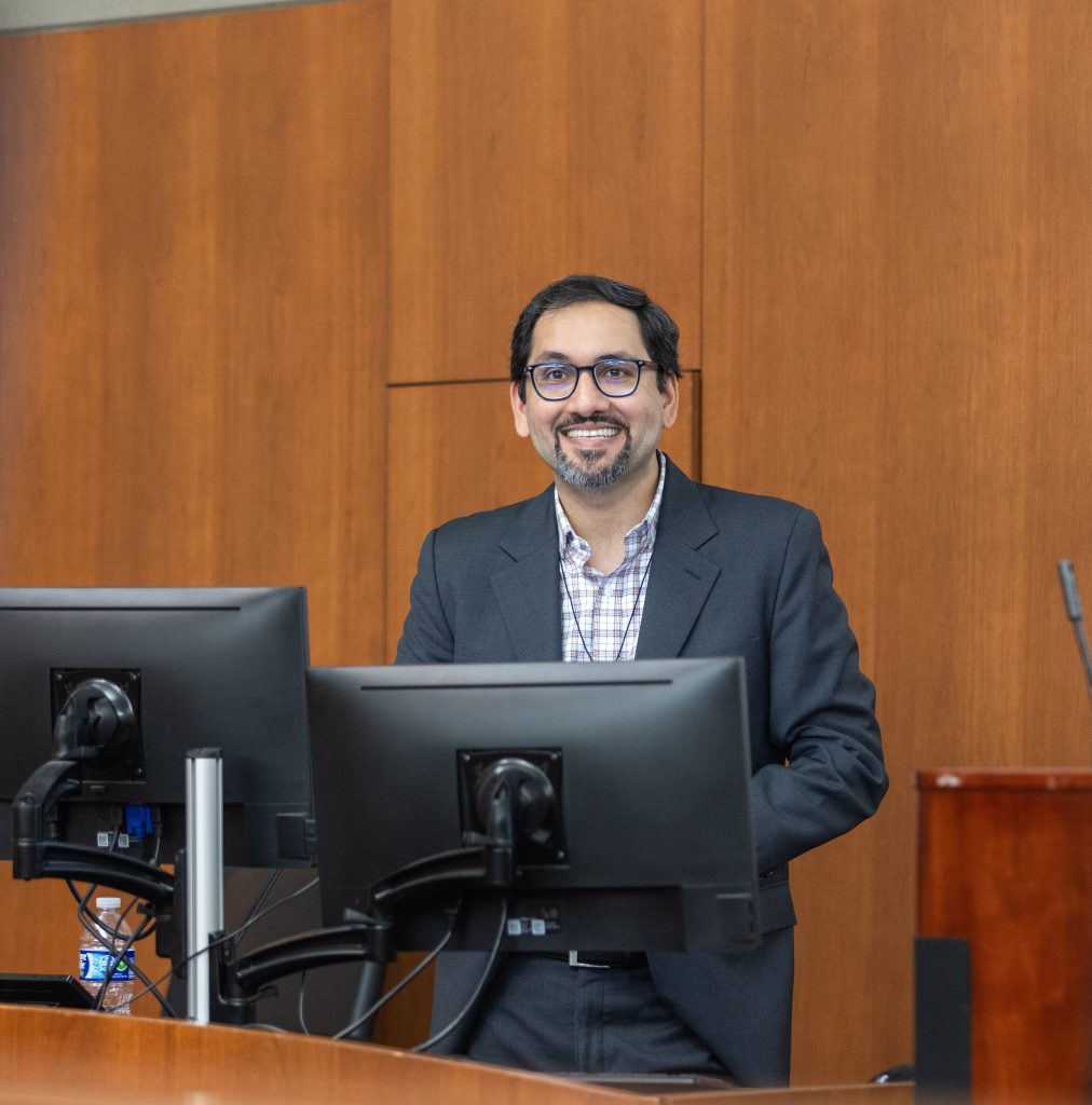 Dr. Murtaza smiling standing at the lectern giving the Precision Medicine Symposium 2025 keynote introduction.