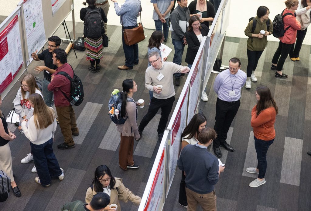 An overhead view of dozens of people looking at and discussing scientific posters at the Precision Medicine Symposium 2025