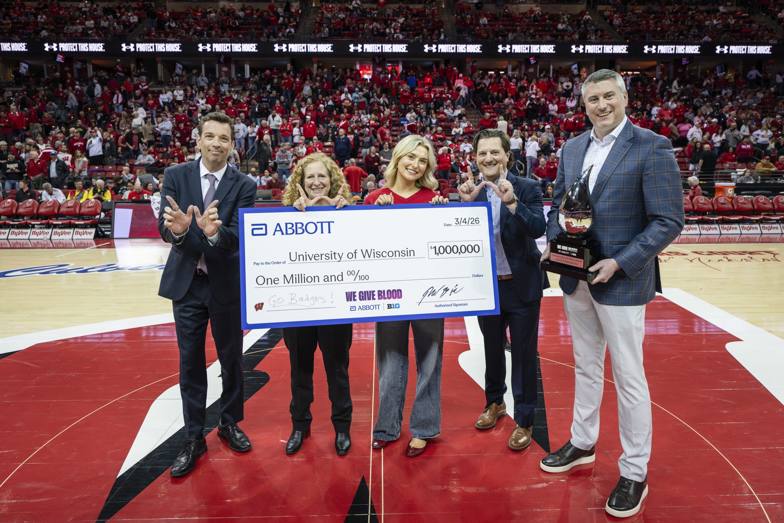 Chairman and CEO of Abbott, Robert Ford, UW–Madison Chancellor Jennifer Mnookin, Student Ambassador of “We Give Blood” Drive, Kate Hopkins, Deputy Athletic Director and Chief Revenue Officer of Wisconsin Athletics, Mitchell Pinta, and Chief Operating Officer of the Big Ten Conference, Kerry Kenny hold up a giant check for one million dollars, a trophy, and make W hand signs during halftime during the Badger men’s basketball game versus Maryland in the Kohl Center at the University of Wisconsin–Madison on March 4, 2026.